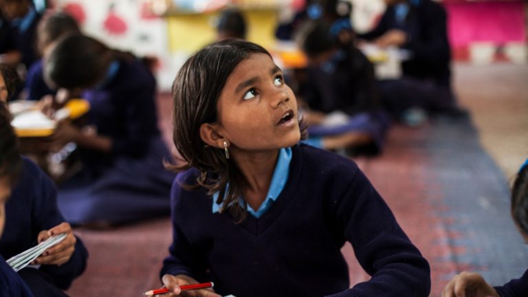A schoolgirl in India looks up at a figure that is out of view