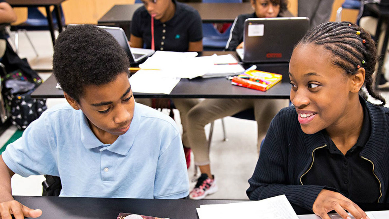 A smiling girl looks at a boy who is reviewing a paper on a school desk in an education setting that uses data