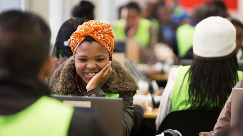 A worker with Harambee Youth Employment Accelerator smiles as she looks at a computer
