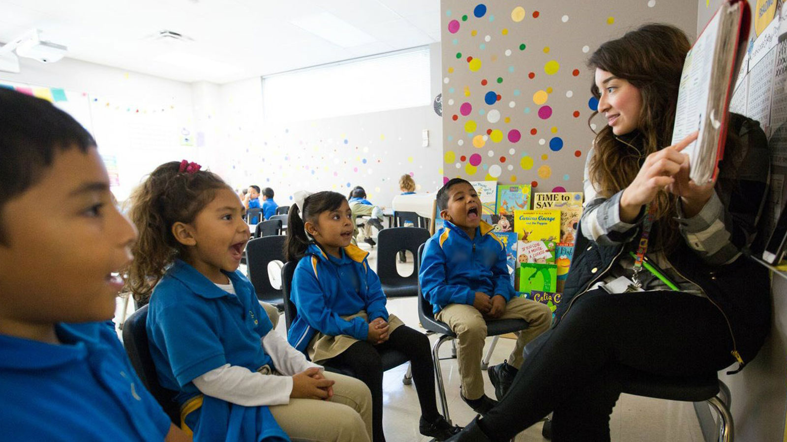 An educator teaches four elementary students in blue polo shorts.