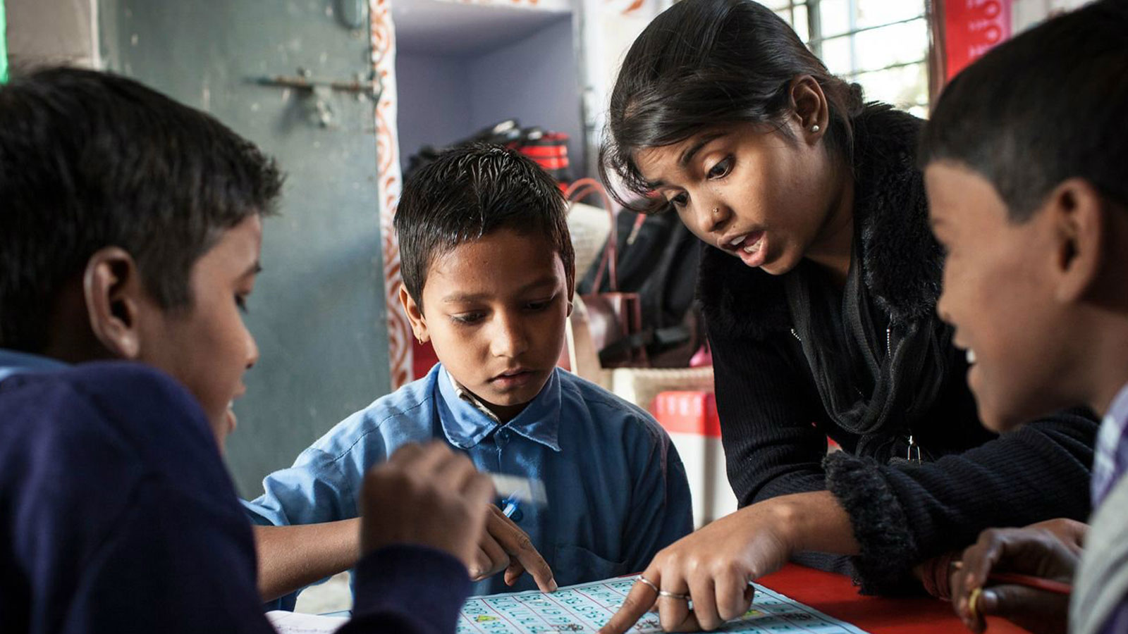 A schoolteacher in India goes over an assignment with three boys