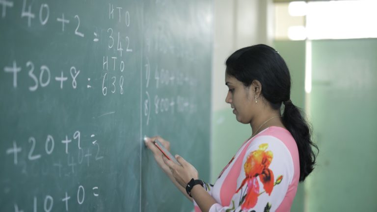 A teacher in India at a chalkboard uses ClassKlap to instruct her students.