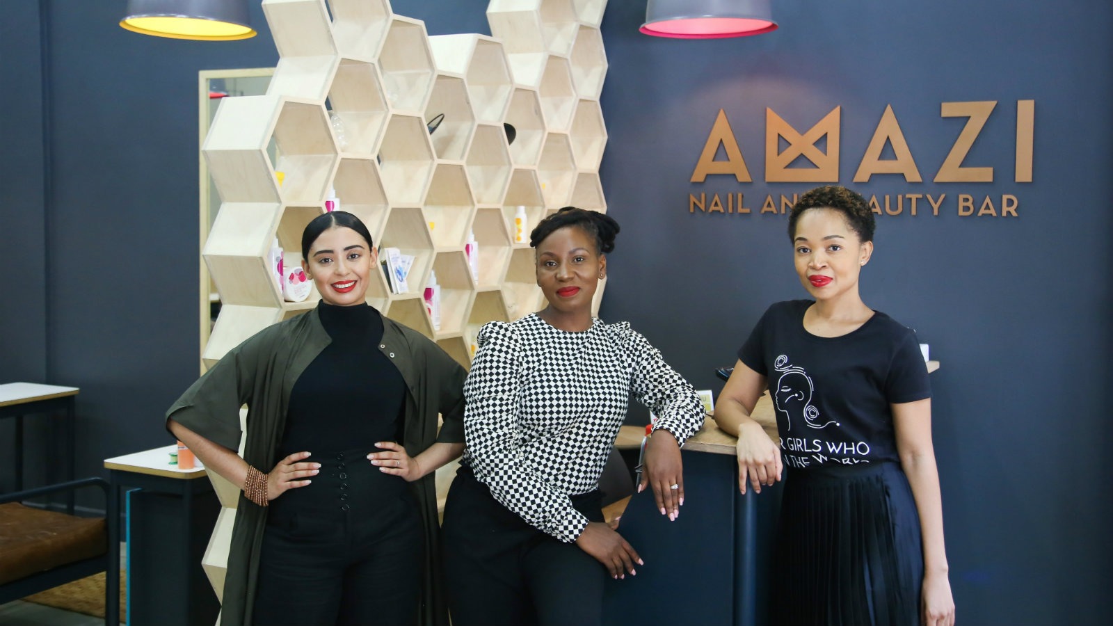 Three women stand in front of the Amazi front desk.