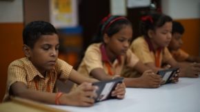 A young man in India completes schoolwork using an electronic device.