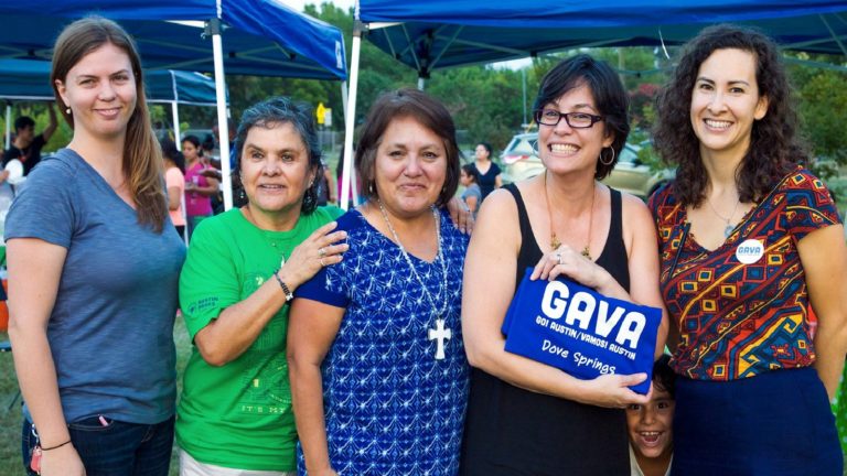 Five women stand together; one is holding up a GAVA sign