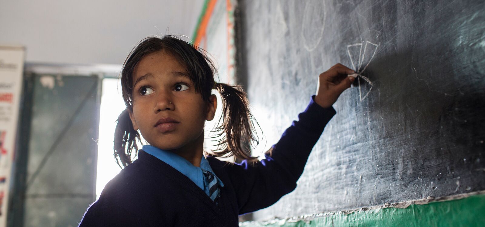 Indian girl writing on a chalkboard in a classroom