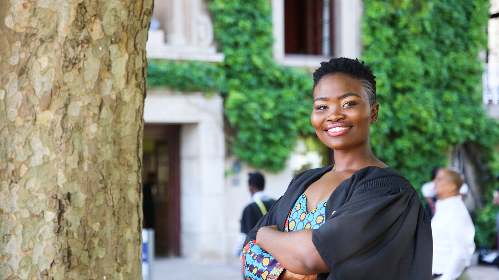 A Dell Young Leader stands outsider her university in a graduation gown