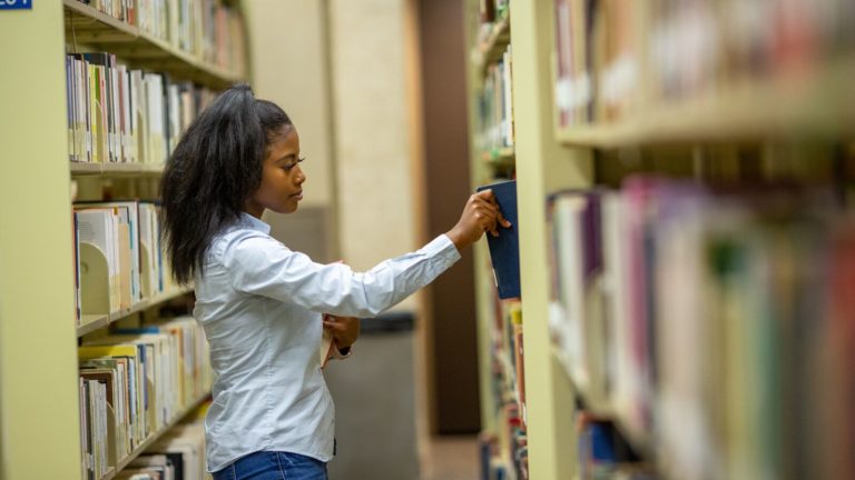 A young woman puts a book on a shelf in a library