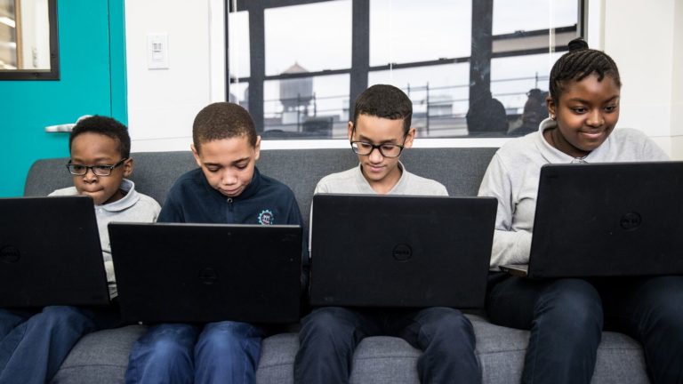 Four students work on computers, sitting on a couch