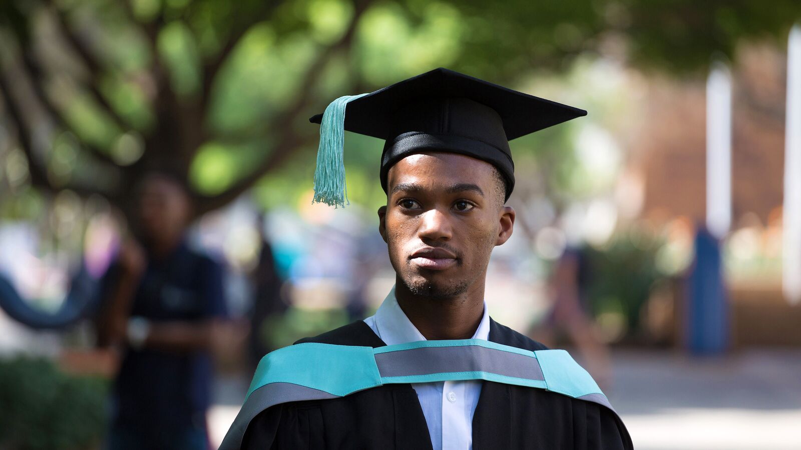 A student in South Africa stands outside in his graduation regalia