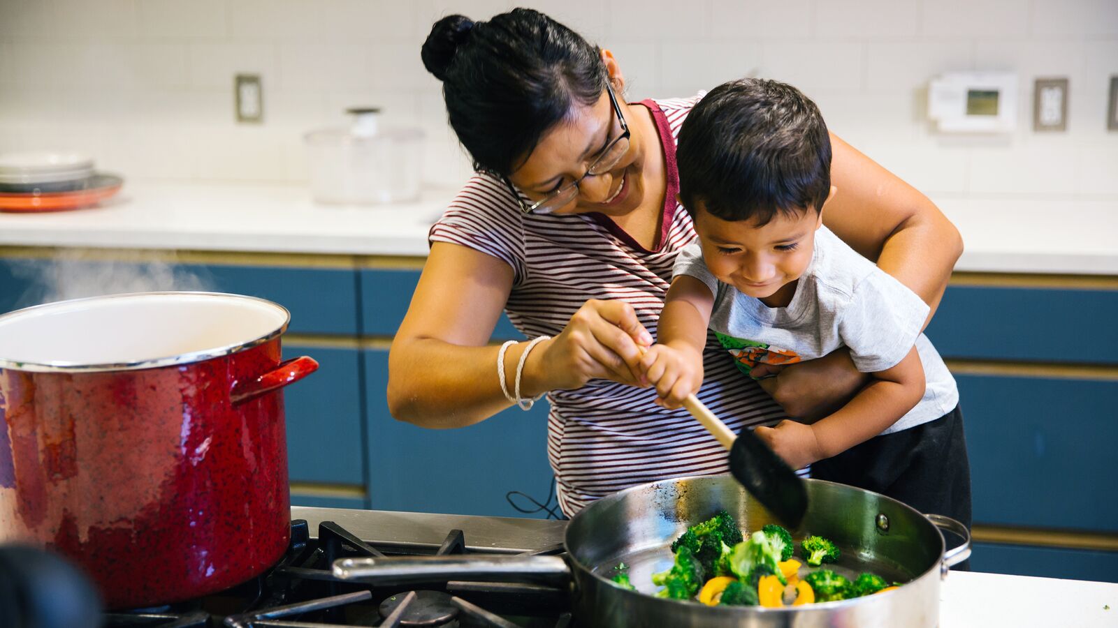 A woman cooks vegetables with her child