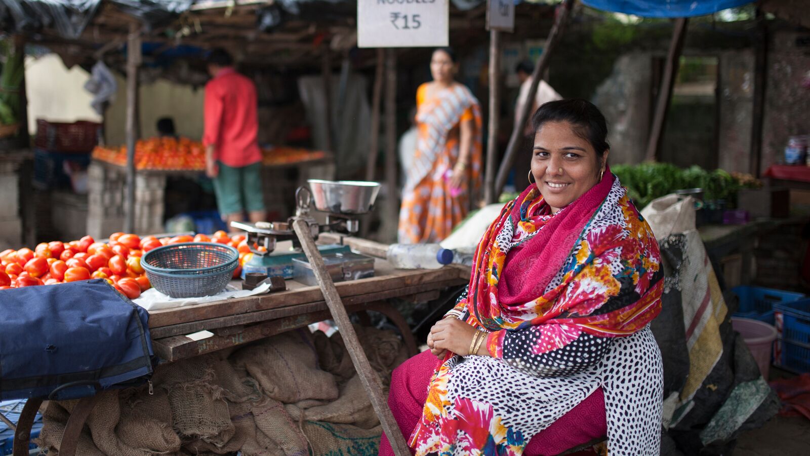 A Svasti customer sits in front of her vegetable stall in an Indian market.