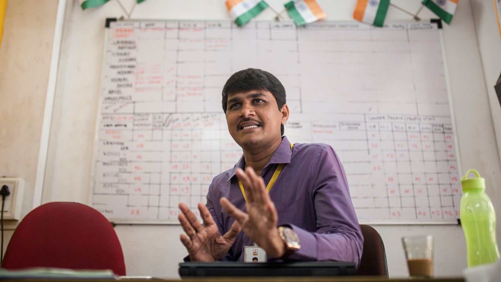 A Svasti manager in a purple shirt sits at a desk in India holding up two hands.