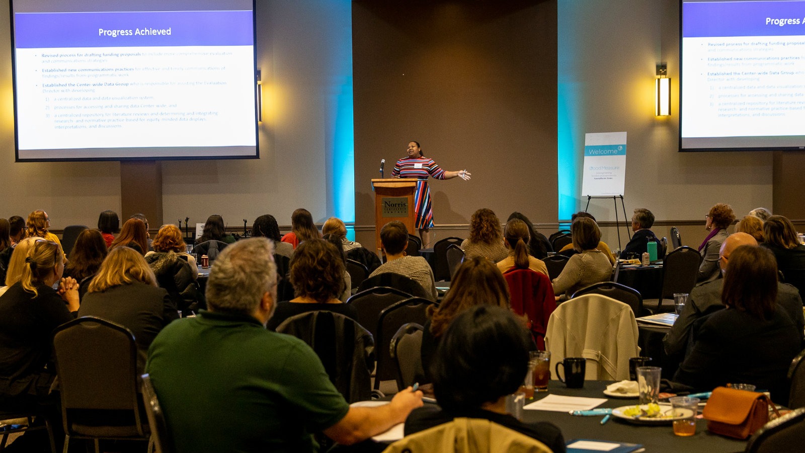 A woman speaks to a large crowd in a conference setting