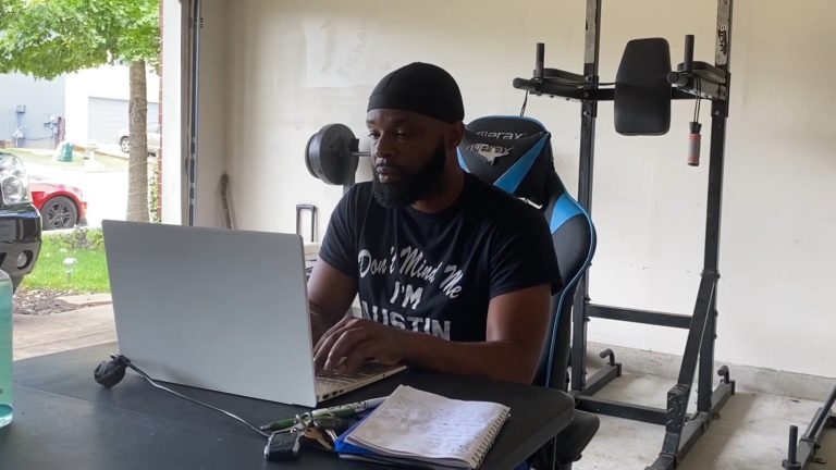 A PelotonU adult learner sits at a computer in his garage