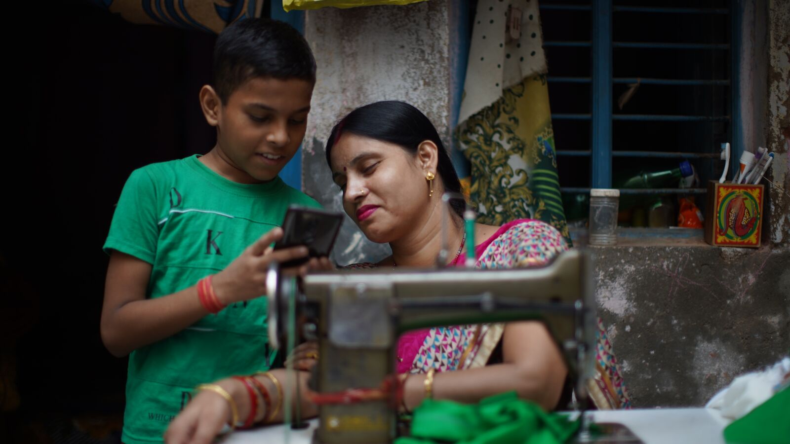 A mother and son in India look at the son's school work on a phone