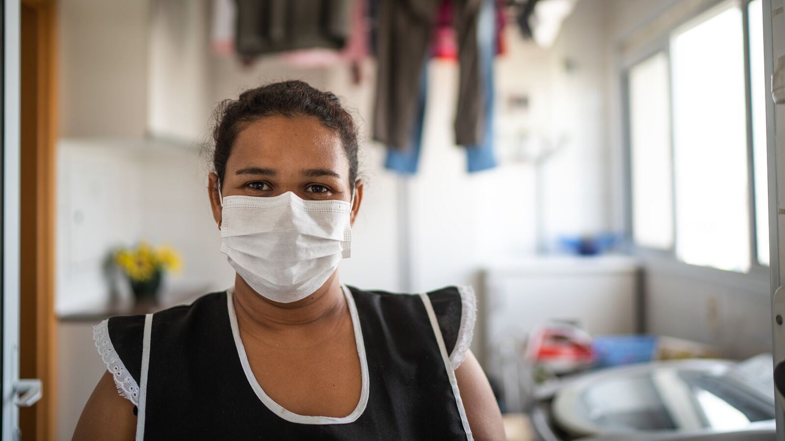 An essential worker stands in a laundry room wearing a mask