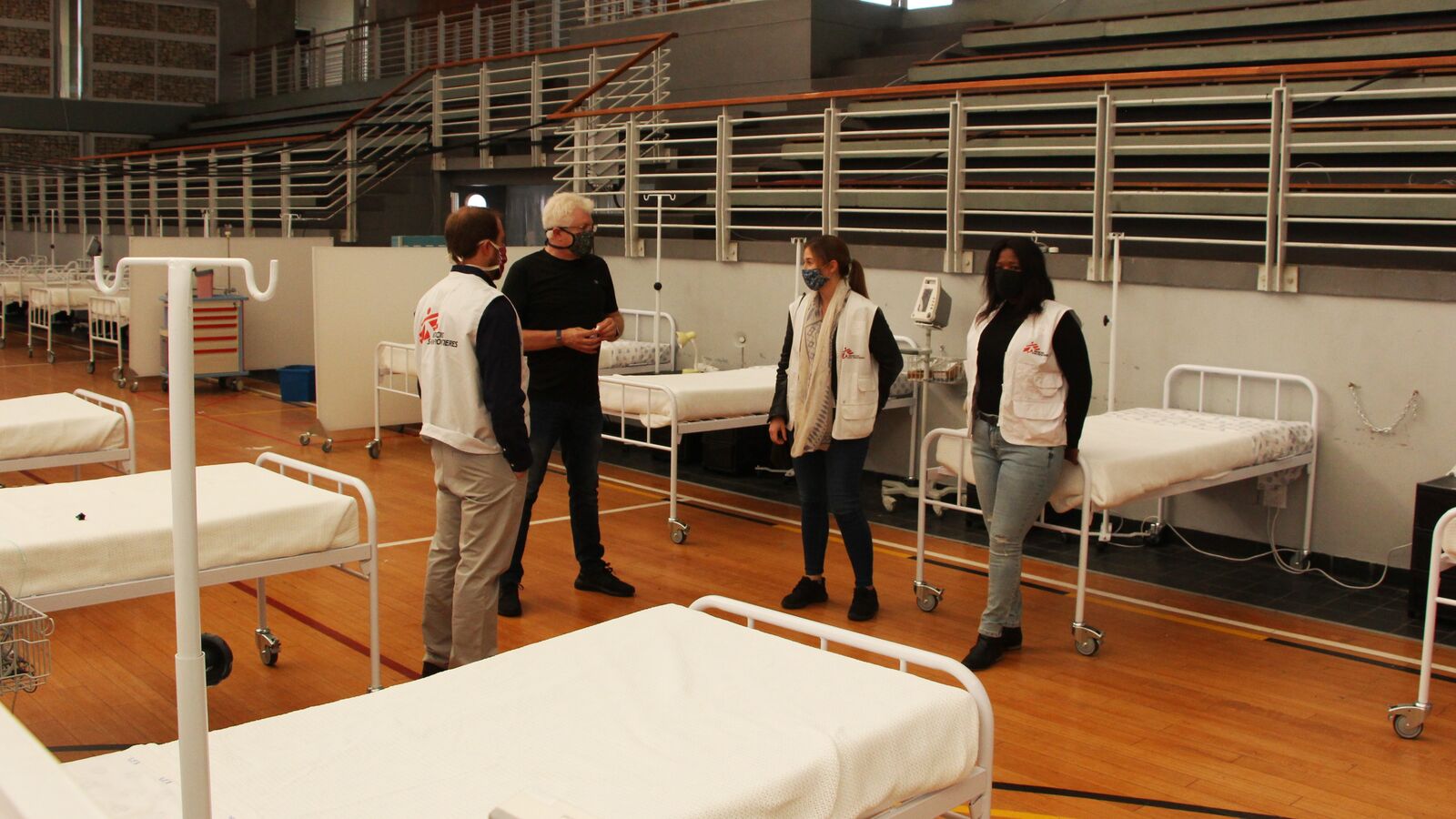 Four healthcare professionals stand talking amid empty beds in the Khayelitsha Field Hospital created by Doctors Without Borders