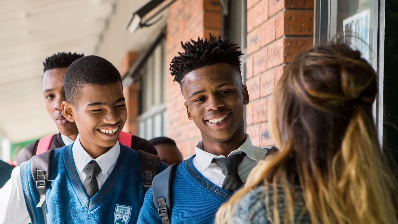 Several students in uniforms stand outside Apex High School, a no-fee public school supported by Acorn Education