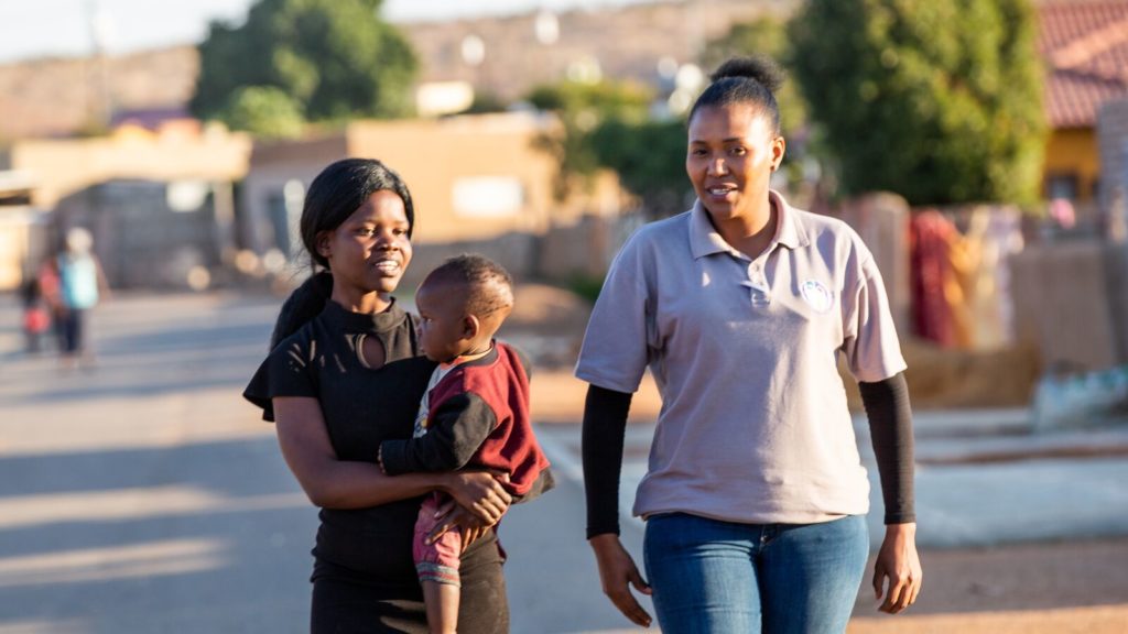 A Mothers2Mothers worker walks and talks with a woman living with HIV and her child