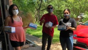 Three volunteers wearing masks prepare to distribute COVID-19 supplies