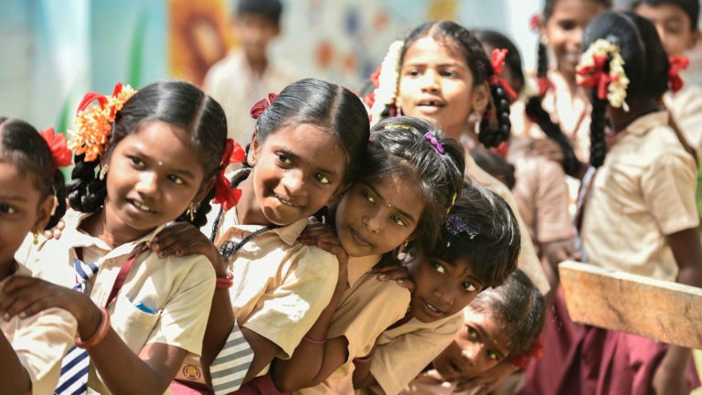 Children in India stand together in a line with smiles on their faces while wearing school uniforms