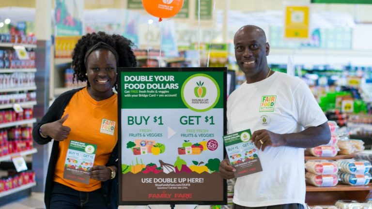 Fair Food Network team members stand by a store sign about a food incentive program
