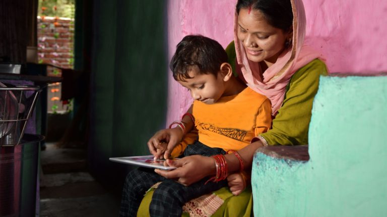 A mother in India helps her son conduct his school work on a digital device