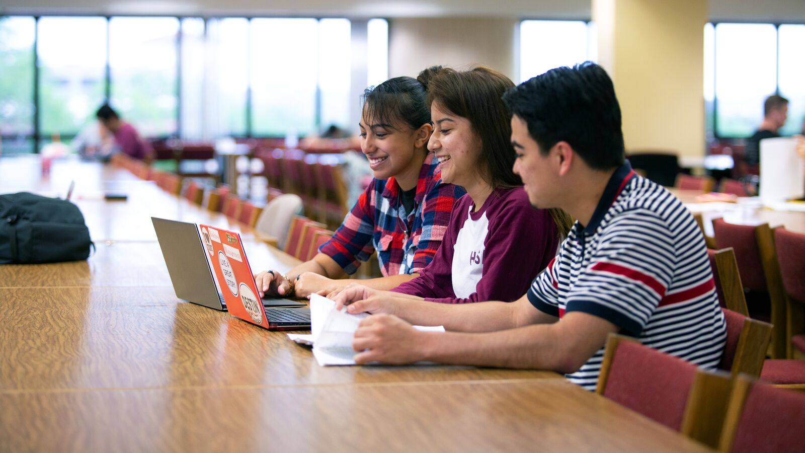 Three students working at a table in a college library, using their computers for virtual support.