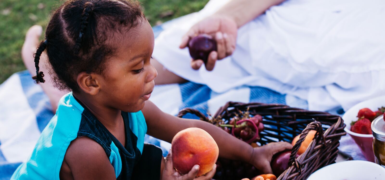 A child holds a peach while sitting on a picnic blanket