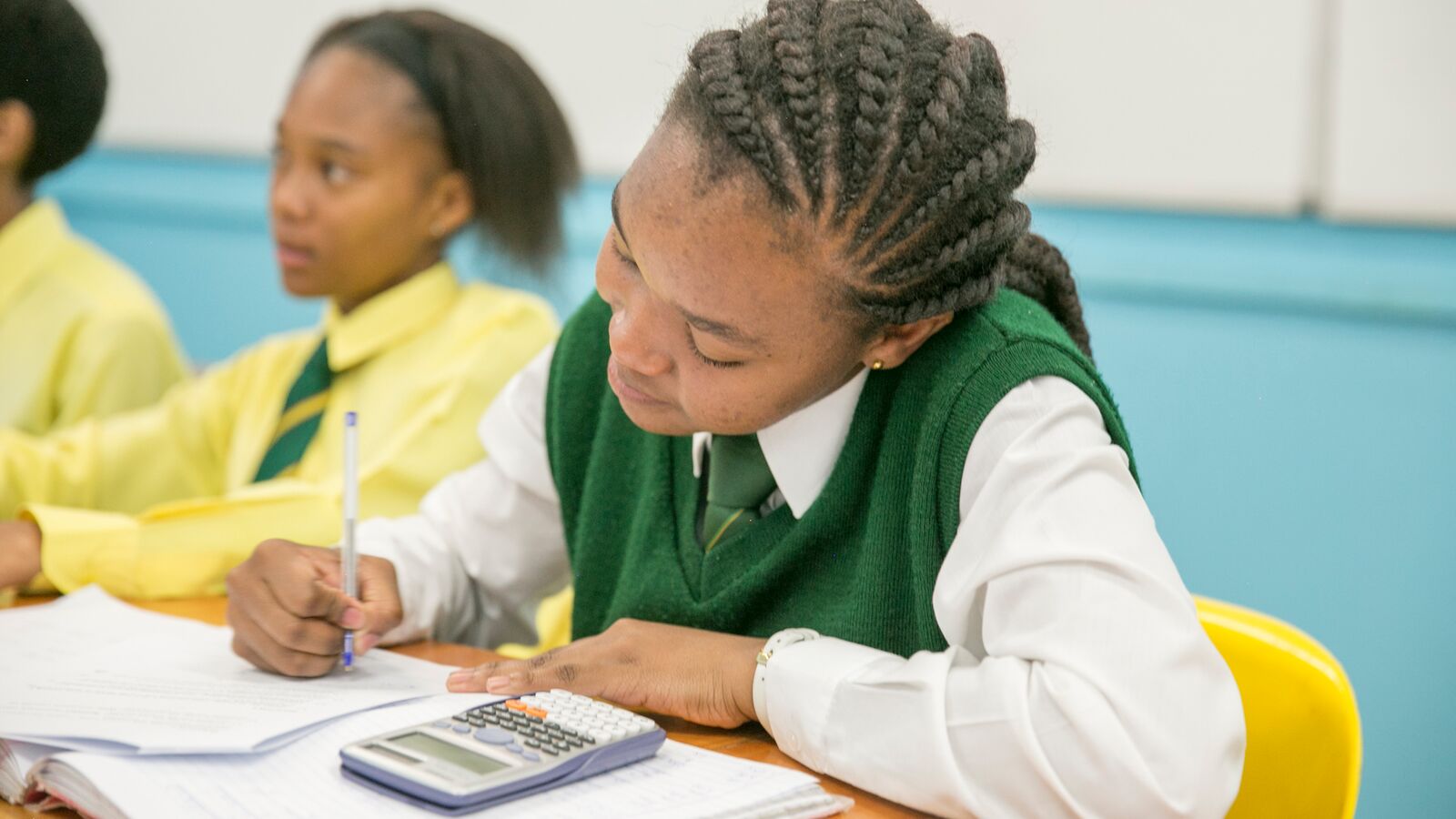 A South African student uses a calculator next to her peer