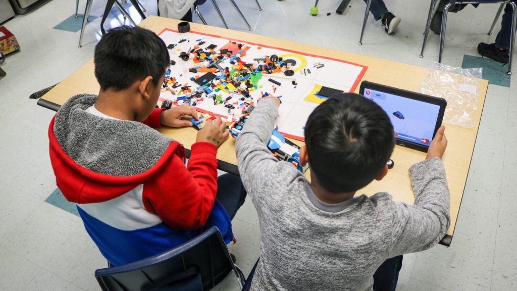 Two Austin Independent School District students sit at a desk and work on building something together using legos 