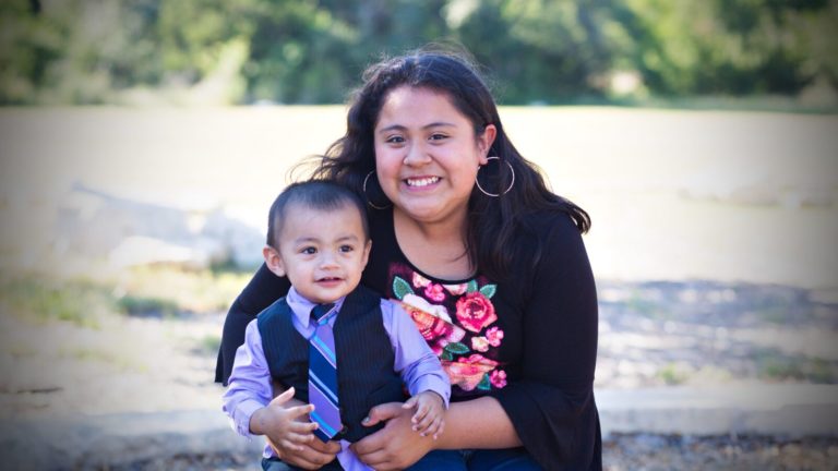 A woman holds a child in her lap and smiles at the camera