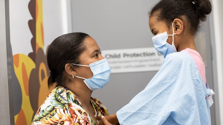 A woman and child stand together wearing masks