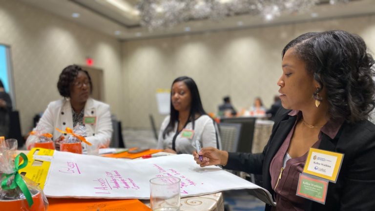 Group of women educators sitting together at a table. One is writing on a large notepad.