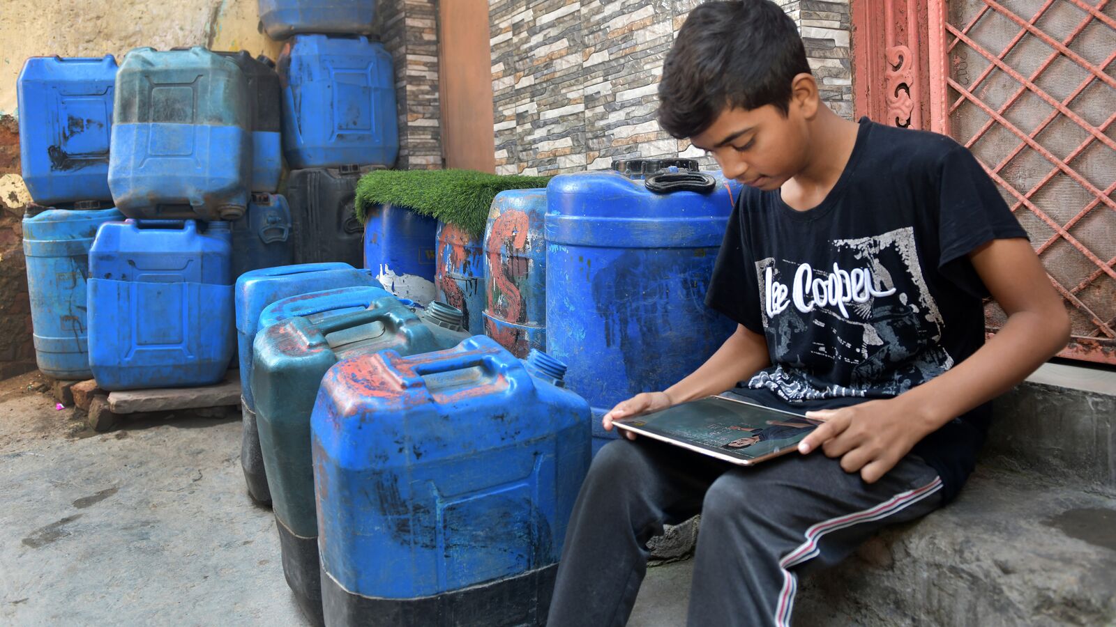 A young Indian boy uses his tablet on the steps of his apartment.