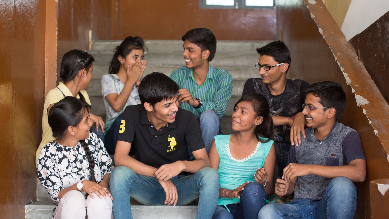 A group of young adults in India sit on their school's steps.