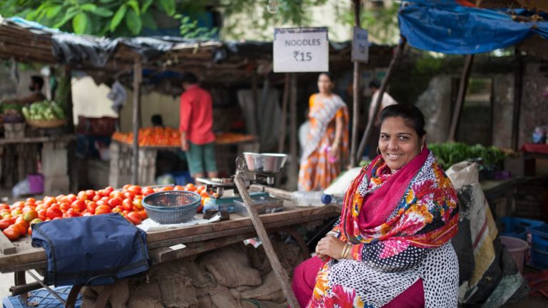 Woman sitting near her food stall, looking into the camera and smiling.