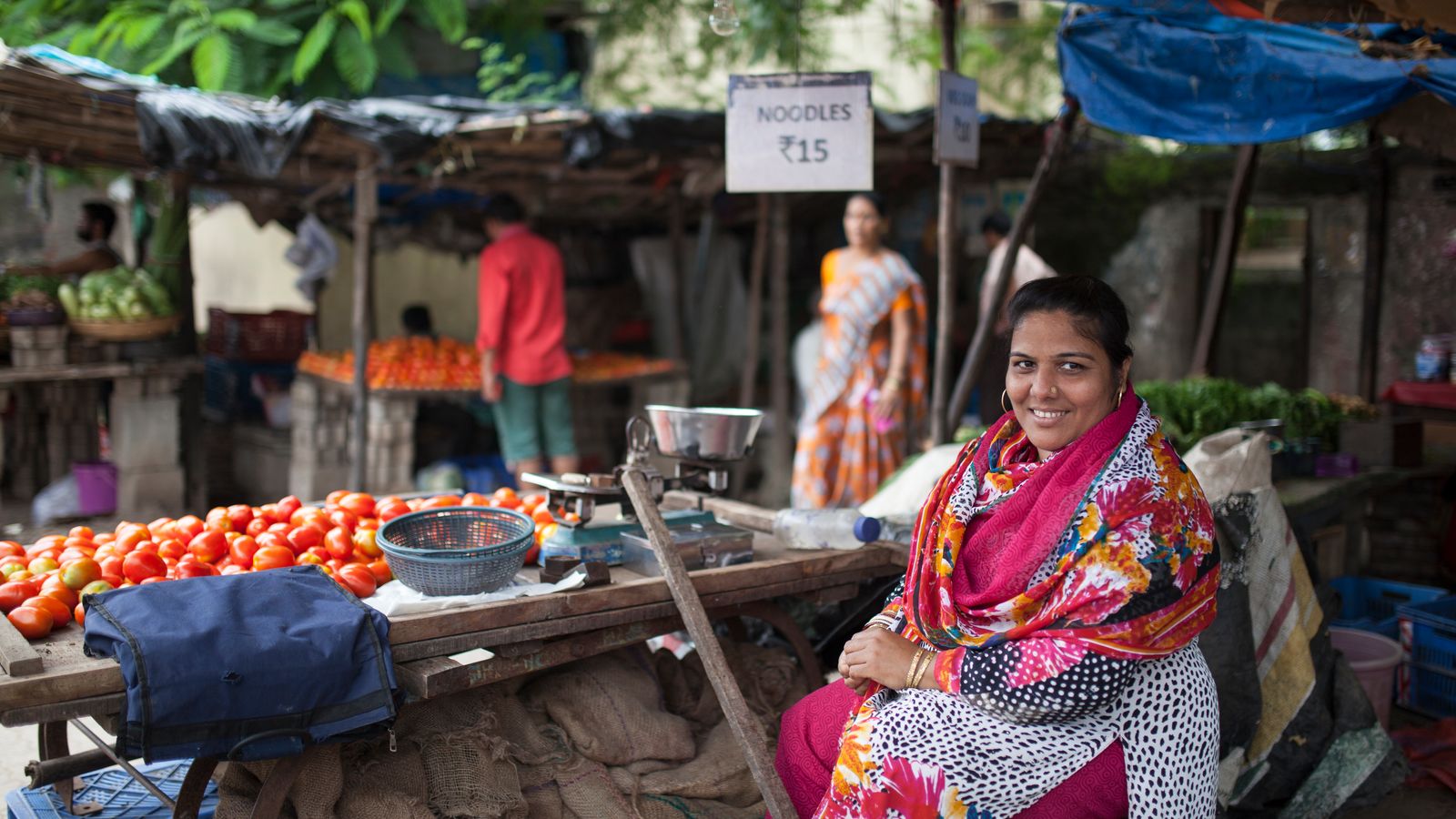 Woman sitting near her food stall, looking into the camera and smiling.