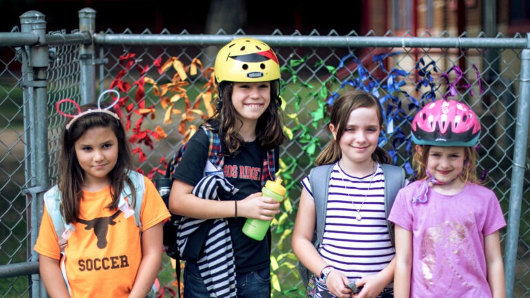 Young girls wearing backpacks smiling in a photo together. Two are wearing bike helmets. Part of the center's STREETS (mobility) and TX SPAN (statewide childhood obesity surveillance) projects.