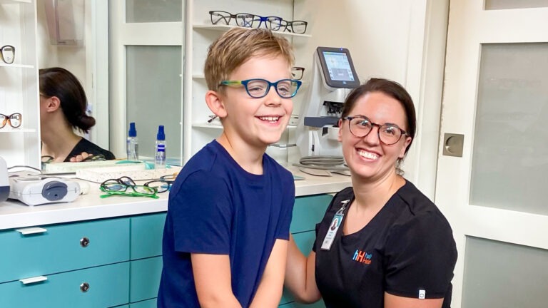 Smiling medical professional wearing glasses with young boy in new glasses in optical Prime.
