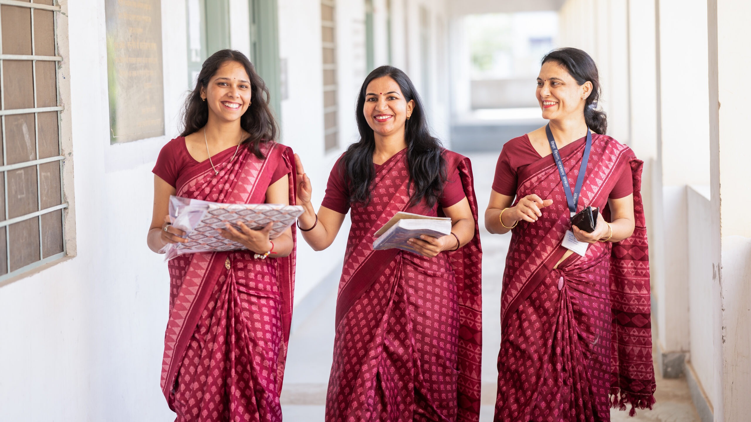 Three teachers at Mahatma Gandhi Government School walking together through the halls smiling.