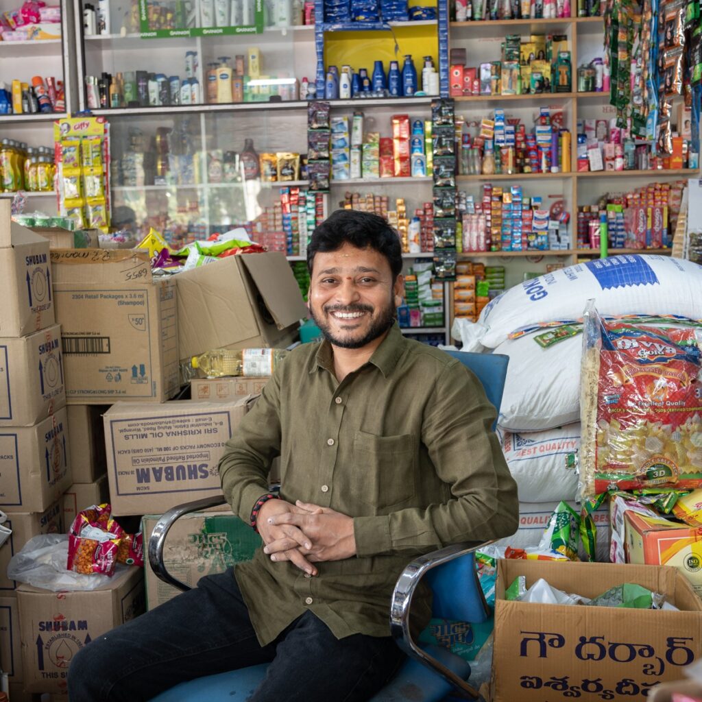 Photo of Vinay, a shop owner, seated among boxes in his place of business. 