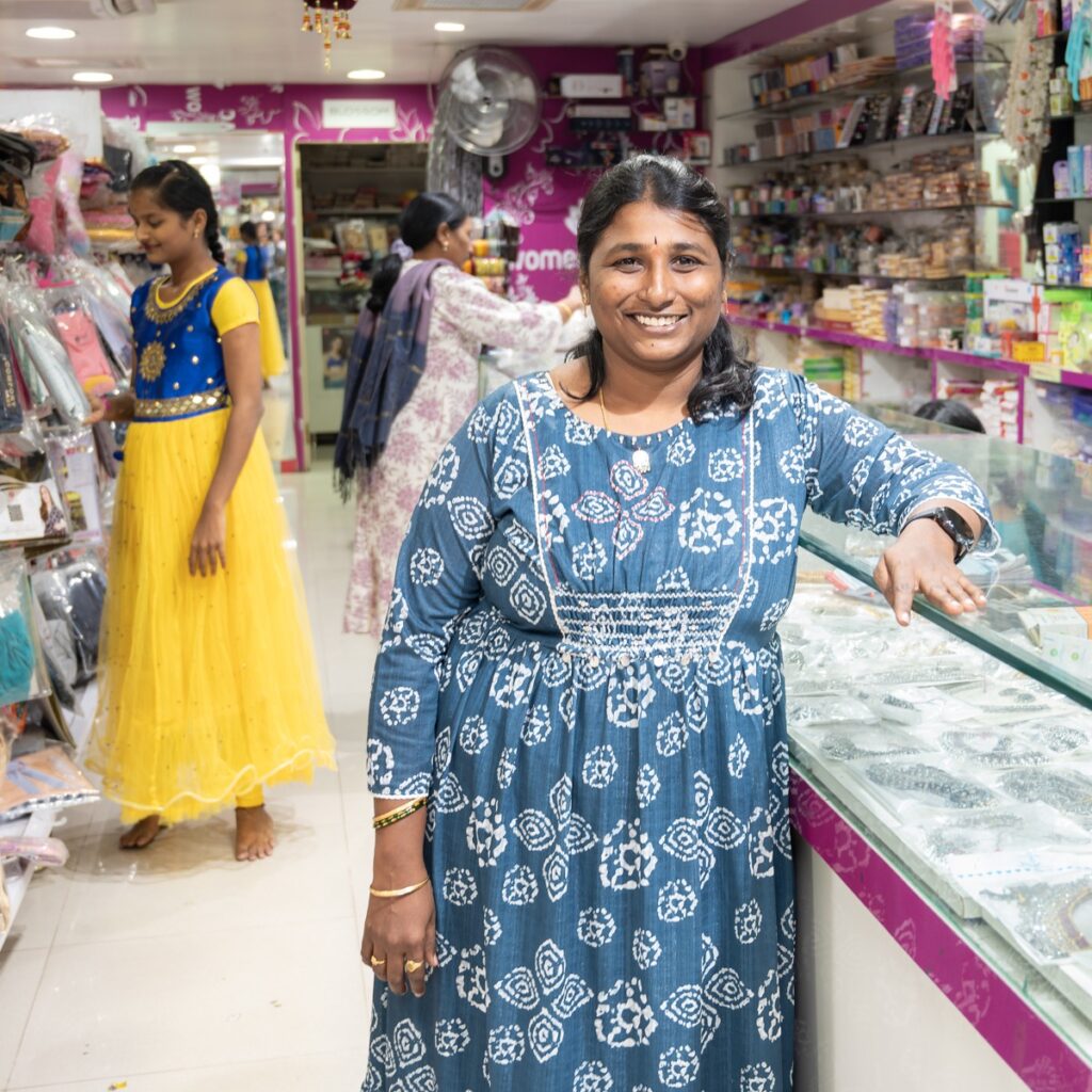 Photo of Swati inside her women's apparel shop, surronded by products and customers.