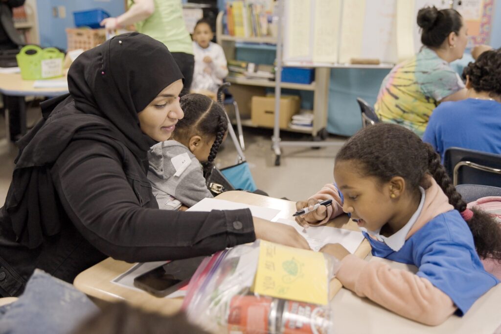 A mother and child work through a reading assignment in a classroom. 