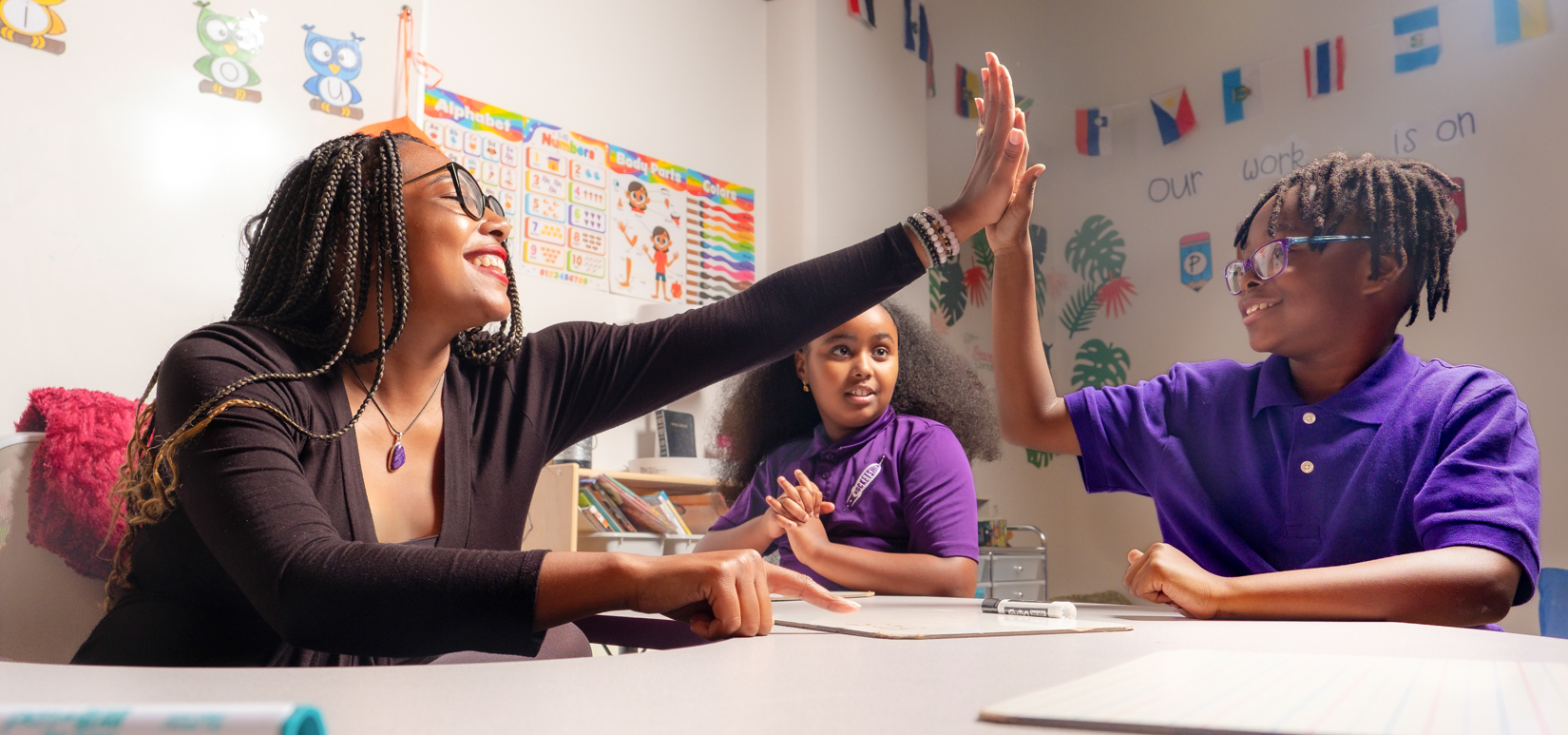 A teacher and student high five in a classroom.