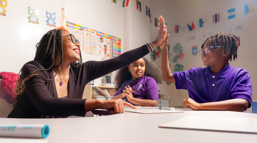 A teacher and student high five in a classroom.