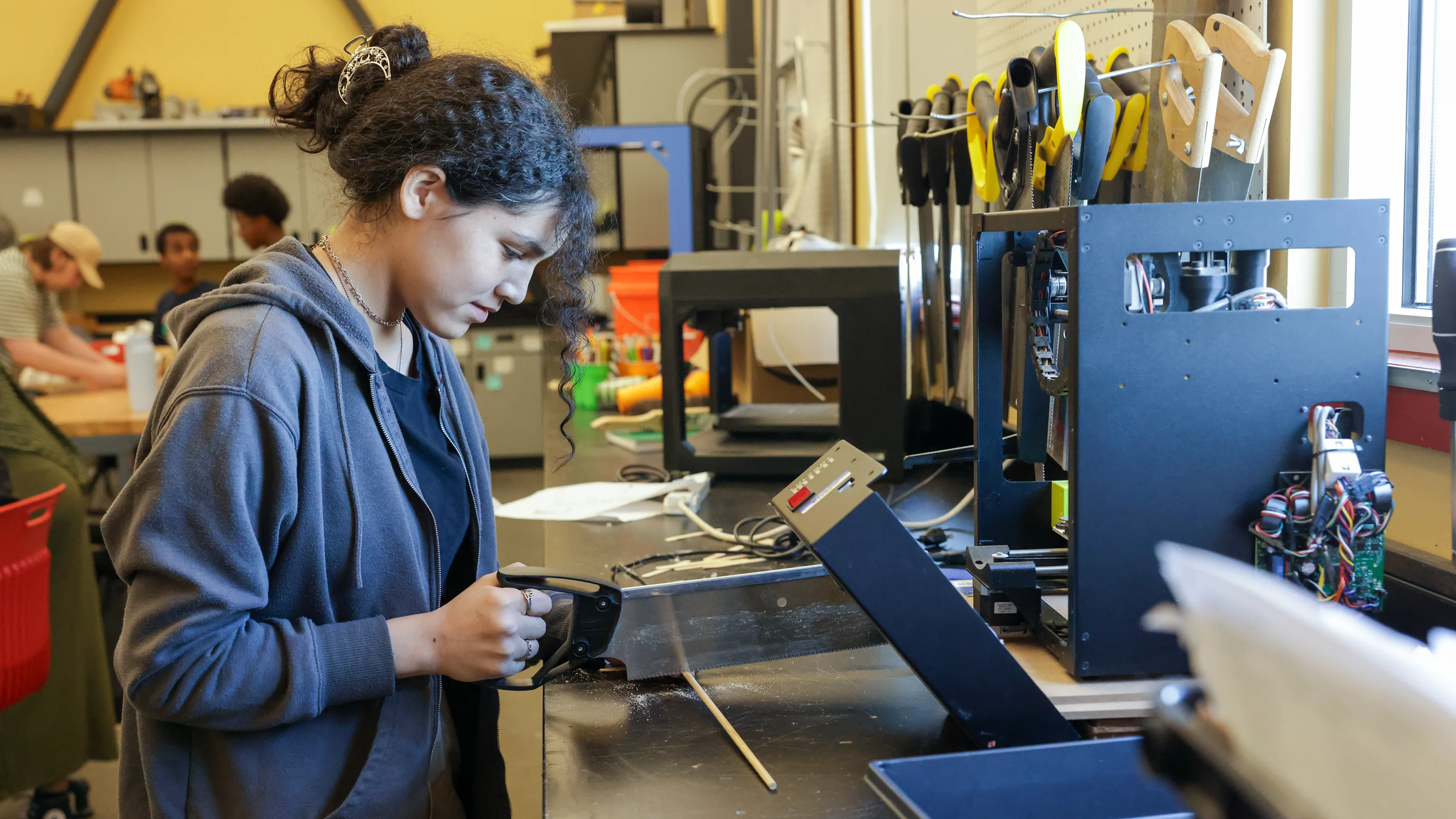 A student saws a piece of wood in a school workshop.