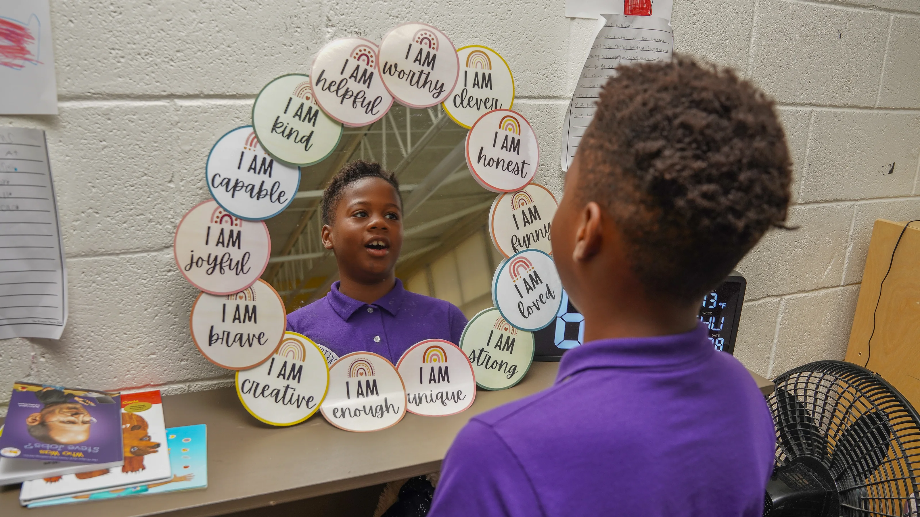 A student looks into a mirror with affirmation messages on post-its framing it.
