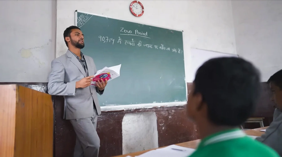 A teacher reads from a textbook in front of a classroom of students.